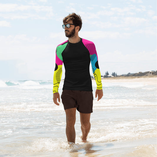 Young guy walking on a beach shore wearing a black men's rash guard with yellow, blues and green sleeves.