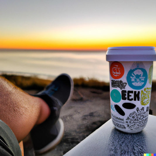 guy sitting down in front of the beach watching the sunset with his white tumbler full of stickers